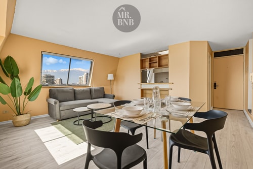 Living comedor con sofá gris, mesa de vidrio con vajilla y planta ornamental
