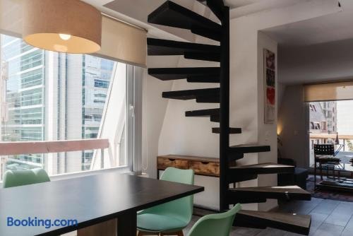 Comedor en dúplex con mesa y sillas verdes junto a escalera caracol negra y ventanal con vista a la ciudad
