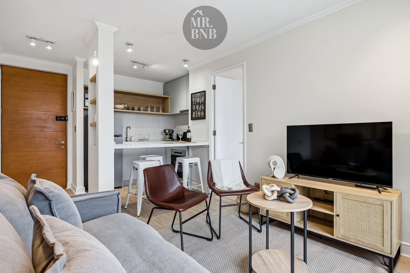 Living con sofá, sillones de cuero, mesa de centro, TV y vista hacia la cocina con barra