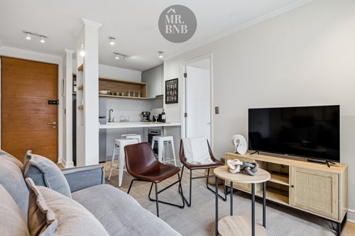Living con sofá, sillones de cuero, mesa de centro, TV y vista hacia la cocina con barra
