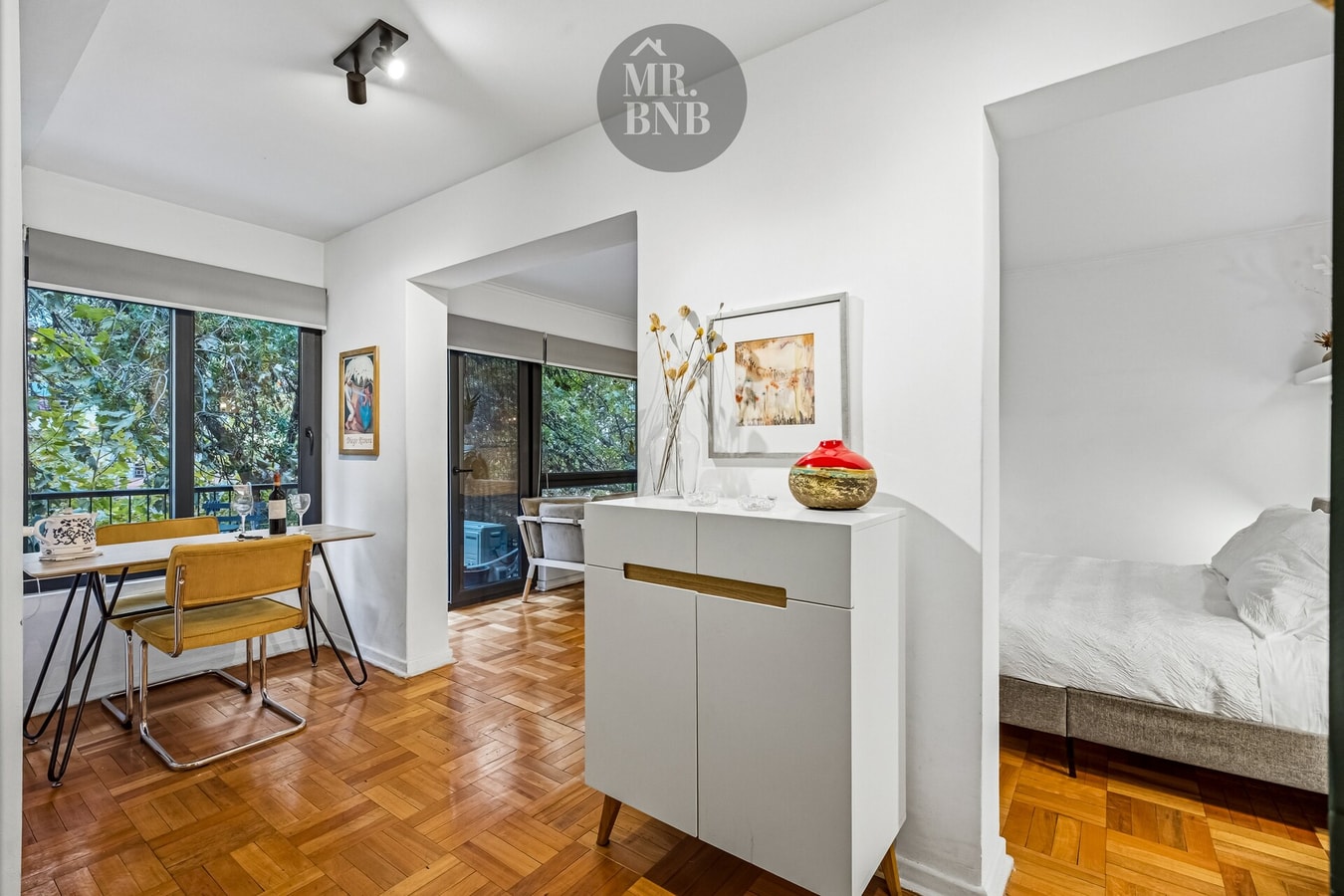 Dormitorio de suite con cama, mesa pequeña y cómoda blanca al fondo