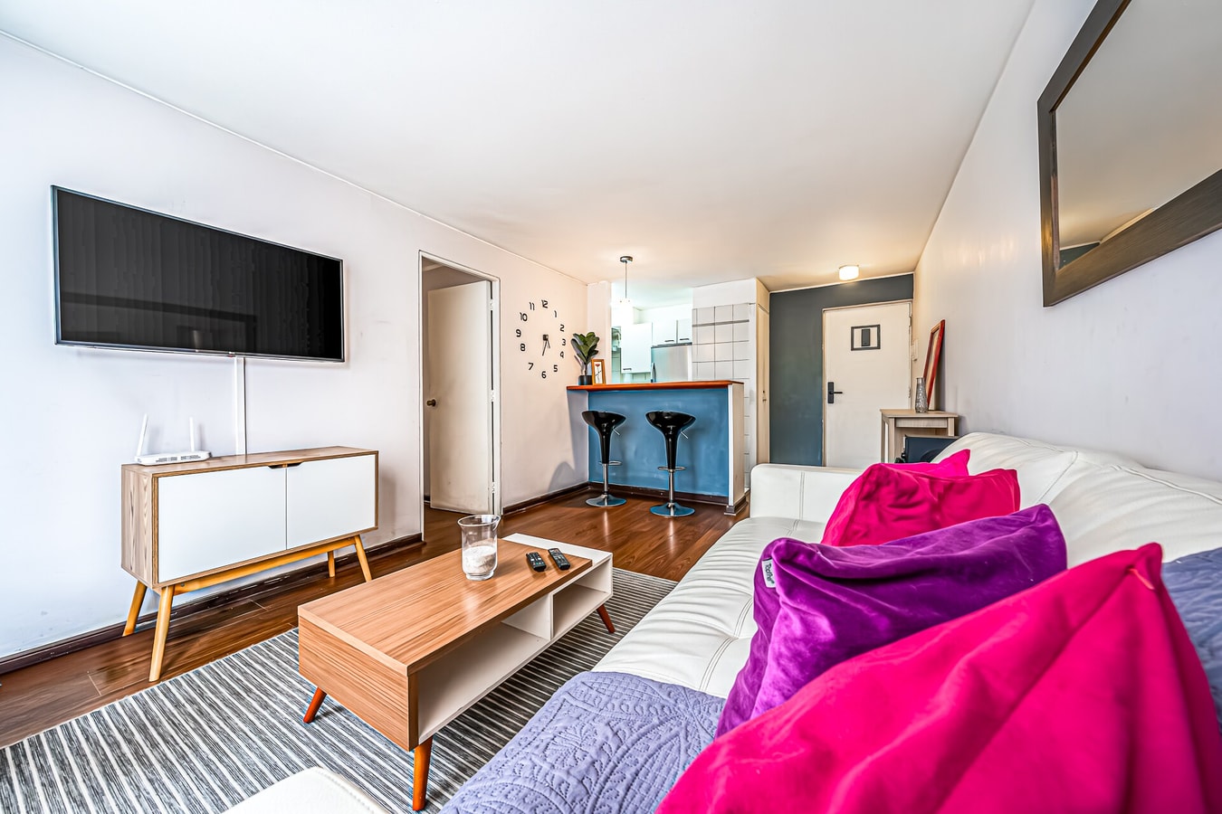 Living comedor con televisor, mueble bajo y sofá con cojín fucsia y morado