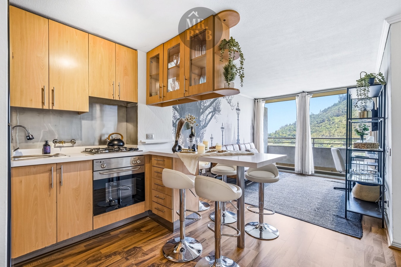 Cocina de madera en L con barra alta y sillas, vista hacia el living con ventanales.