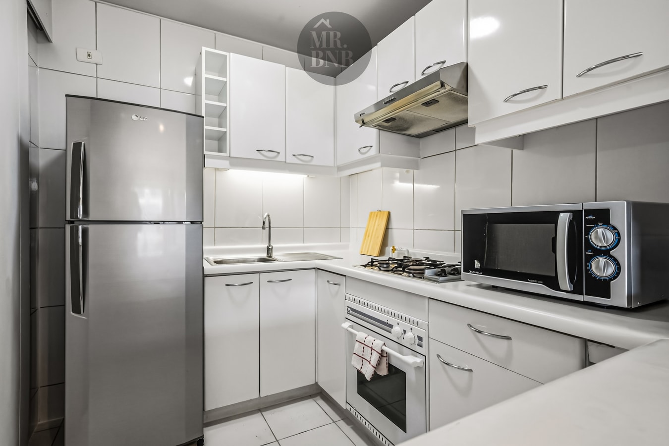 Cocina con refrigerador, microondas, cocina a gas y muebles blancos.
