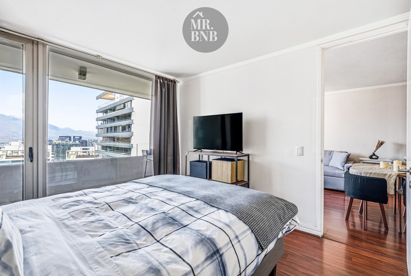 Dormitorio con cama, televisor y living al fondo