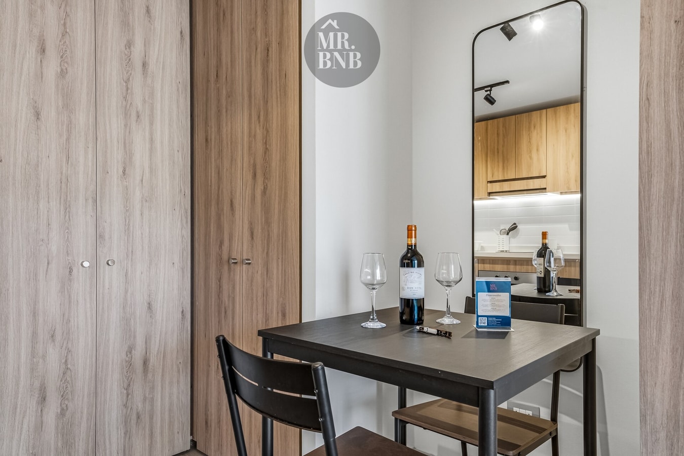 Mesa pequeña con dos sillas y copas de vino junto a un espejo de piso