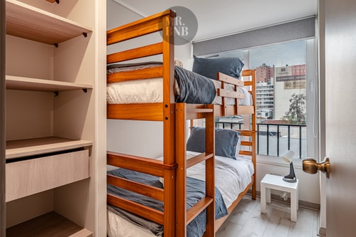 Dormitorio con litera de madera, veladores y clóset abierto con repisas.