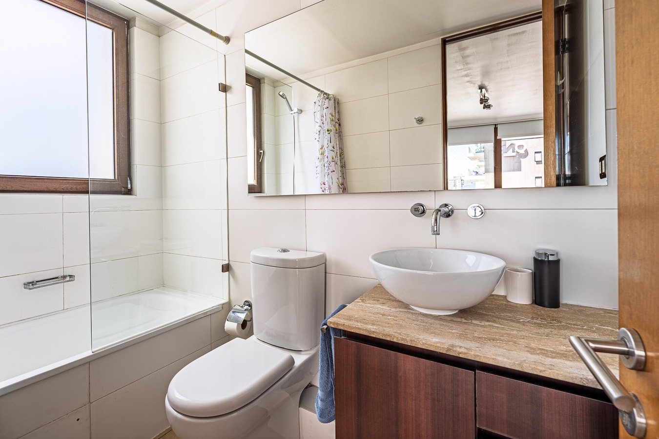 Baño con tina, lavamanos ovalado sobre mueble de madera y espejo