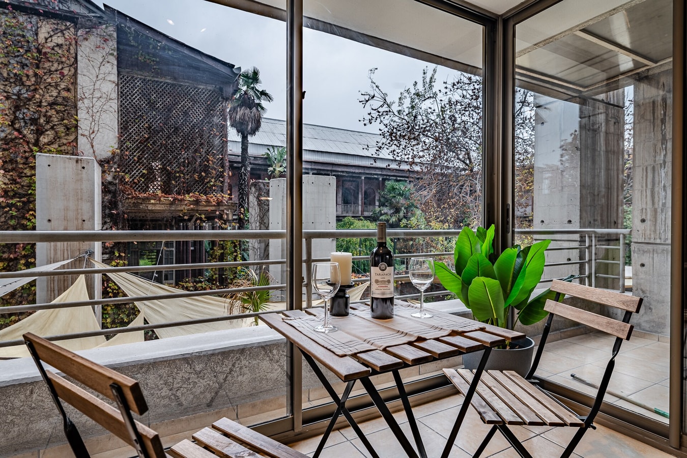 Terraza con mesa de madera, sillas, planta y copas de vino