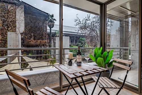 Terraza con mesa de madera, sillas, planta y copas de vino