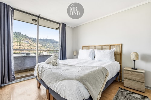 Dormitorio con cama, velador y ventanal con vista al cerro y cordillera.