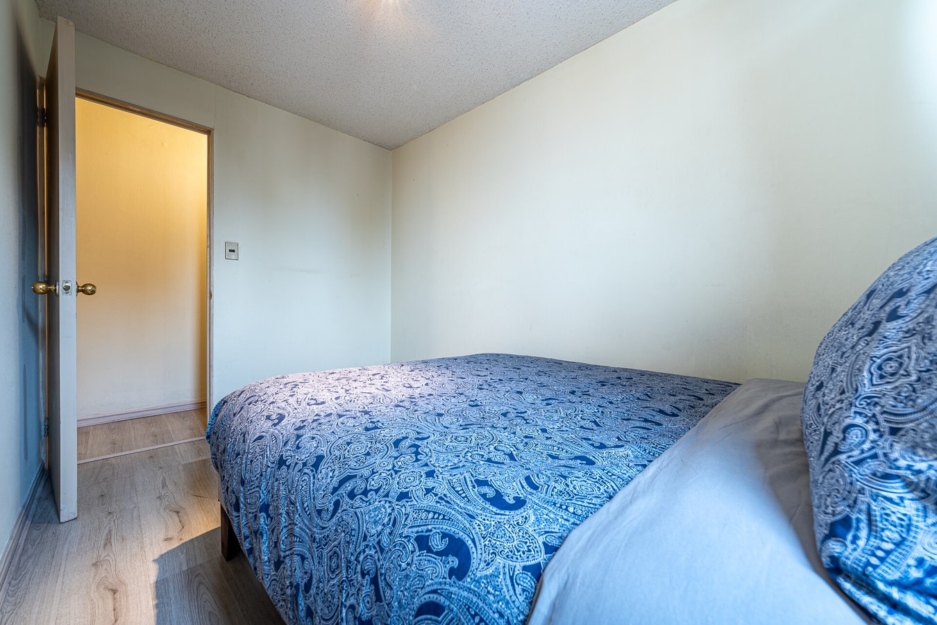 Dormitorio con cama matrimonial con cubrecama azul y puerta hacia el pasillo.