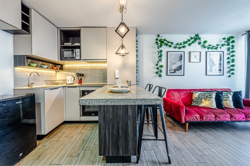 Cocina y living integrados, mesón central con banquetas altas, sofá rojo y decoración con enredadera sobre la pared