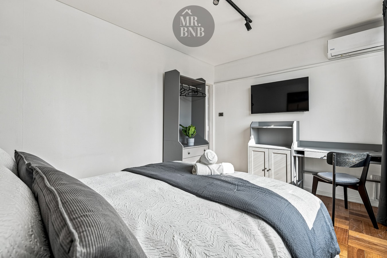 Dormitorio con cama, escritorio con silla, TV en la pared y aire acondicionado