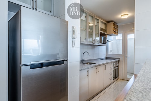 Cocina con refrigerador de acero, muebles blancos y microondas empotrado