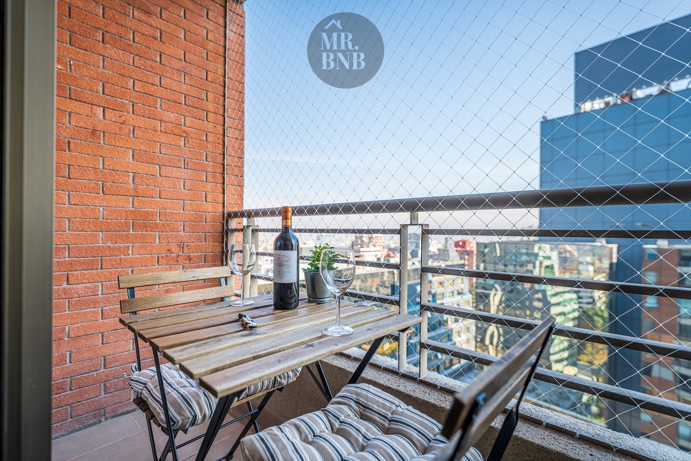 Balcón privado con mesa, dos sillas y vista a edificios de la ciudad