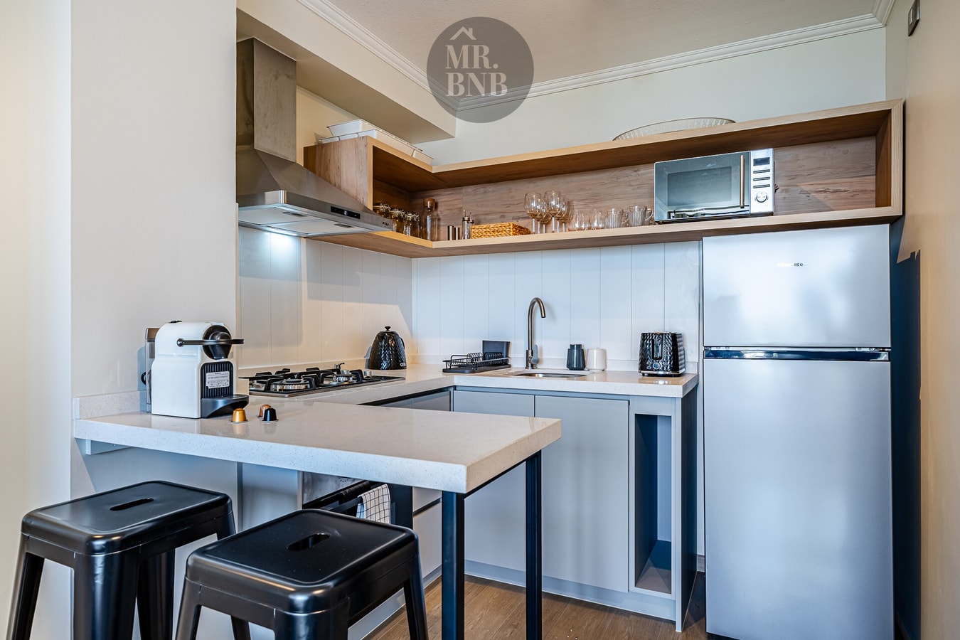 Cocina con barra, banquetas, refrigerador y cafetera de cápsulas