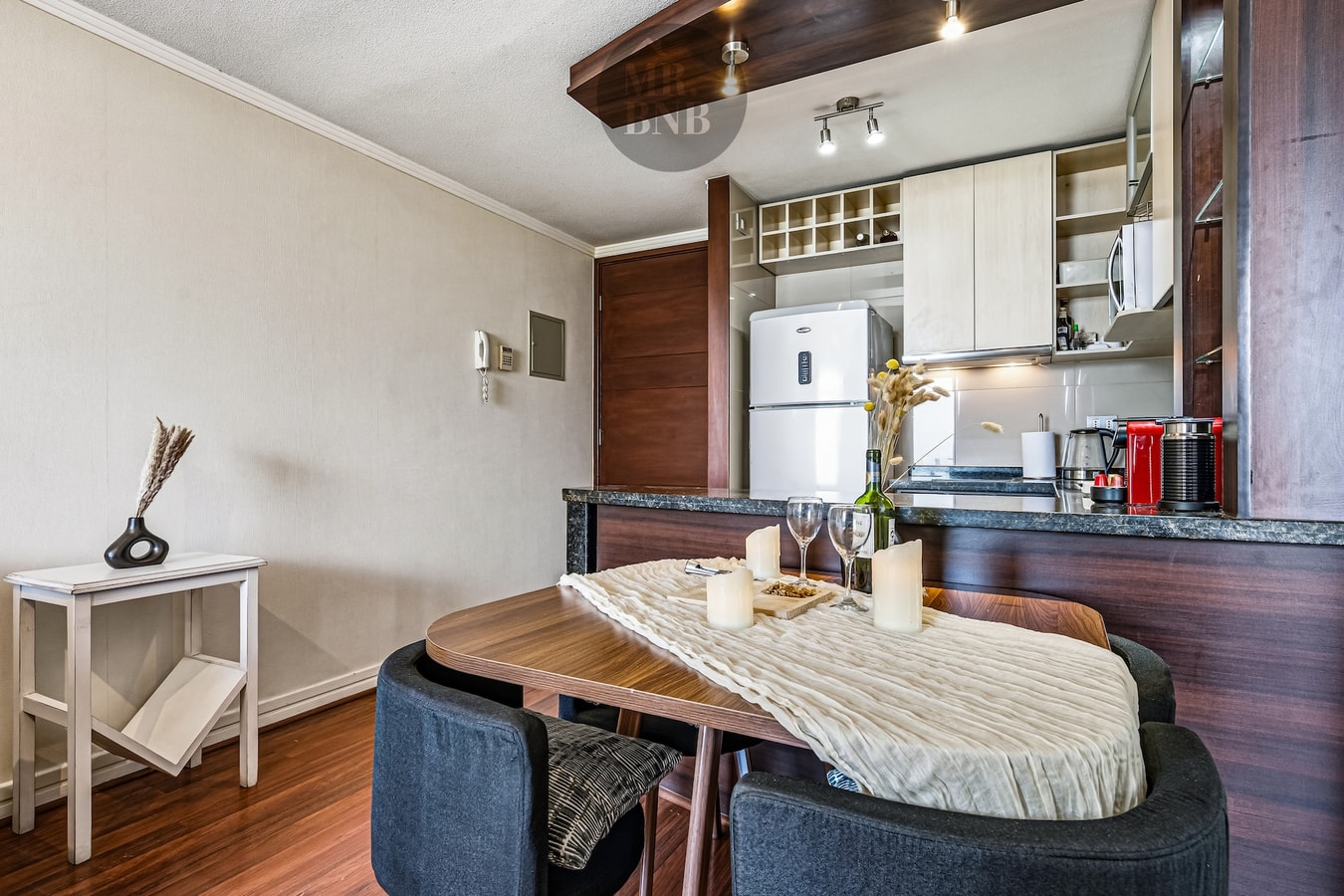 Comedor con mesa de madera, sillas y barra de cocina al fondo