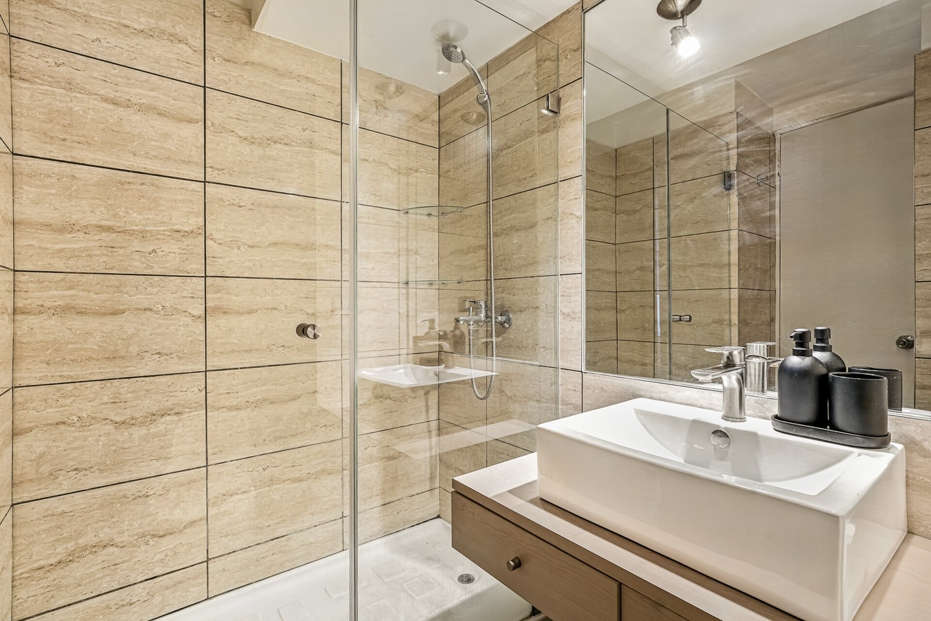 Baño con mueble vanitorio, espejo y ducha de vidrio en tonos beige