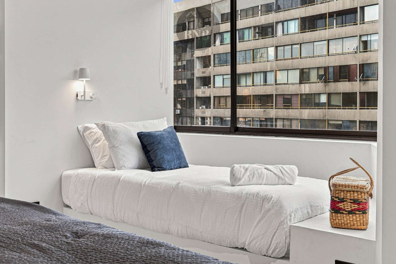 Dormitorio con cama y ventanal con vista a edificios.