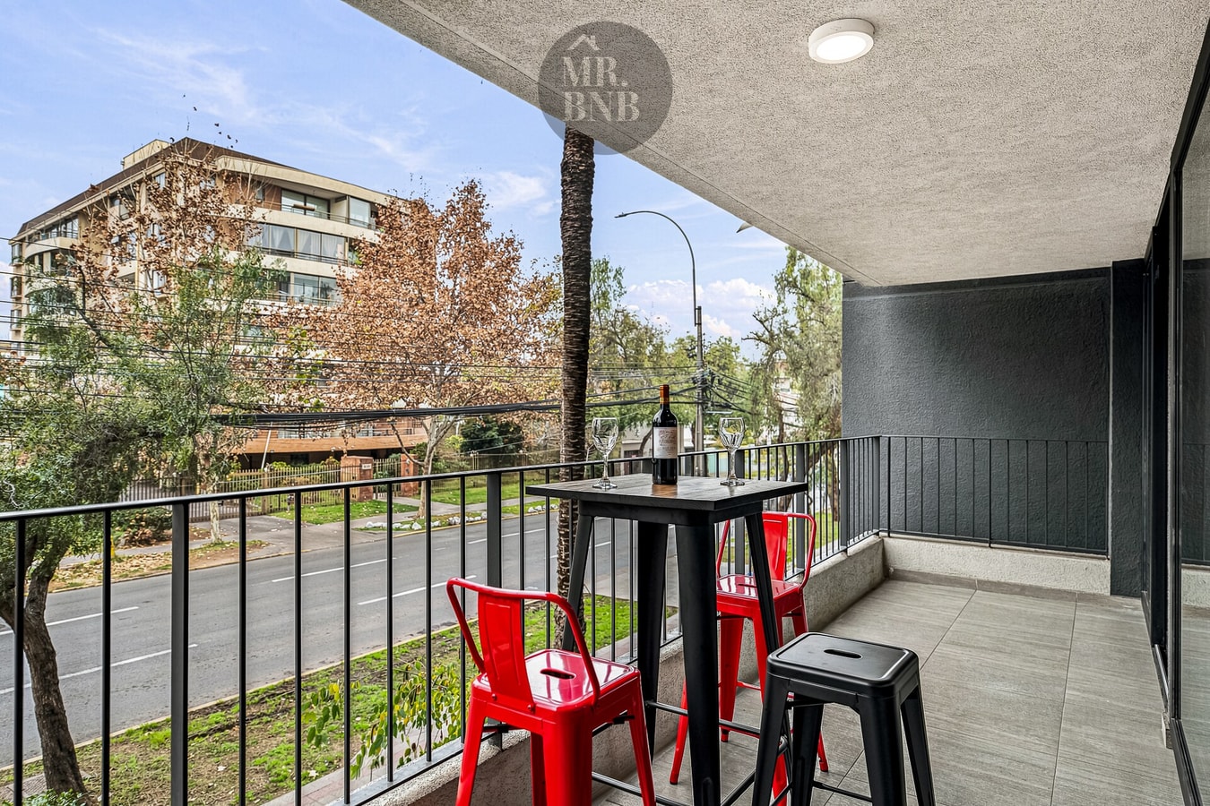 Terraza propia equipada con mesa alta y sillas, vista a árboles y edificios.