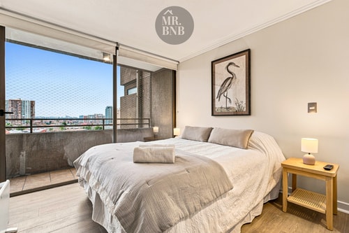 Dormitorio con cama queen, veladores, cuadro de garza y ventanal con vista y acceso a terraza