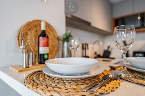 Detalle de mesa puesta con vajilla, copas de vino y mantel individual de fibra natural, sobre la barra de la cocina