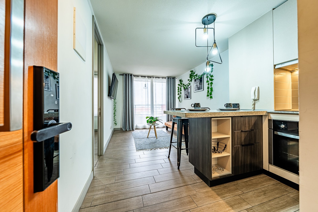 Hall de entrada del departamento con puerta de acceso abierta y vista hacia la cocina con isla de madera al fondo
