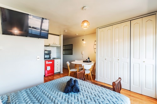 Estudio con cama, televisor en la pared, closet blanco y kitchenette con refrigerador rojo