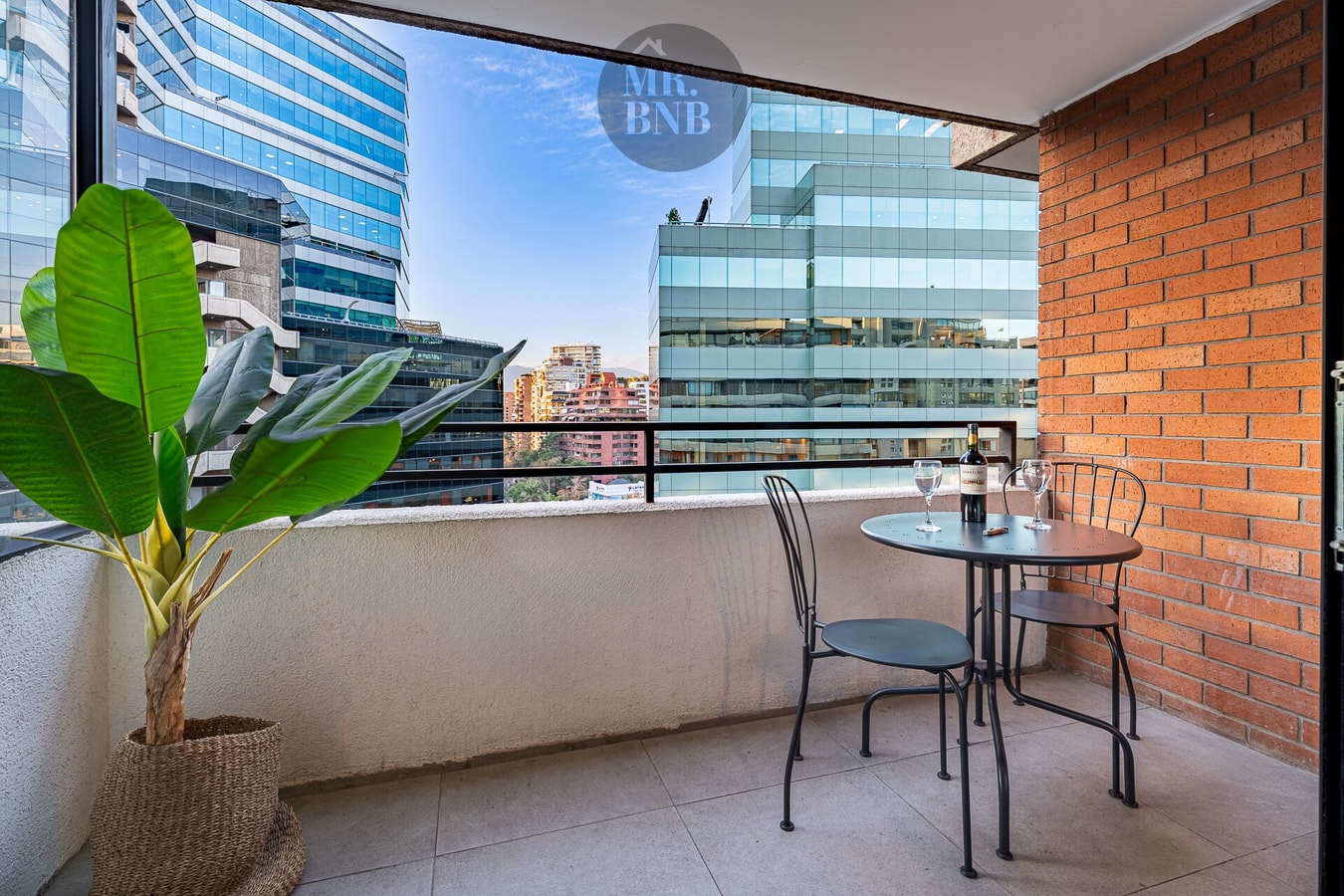 Terraza privada con mesa pequeña y dos sillas, planta y vista a edificios vecinos