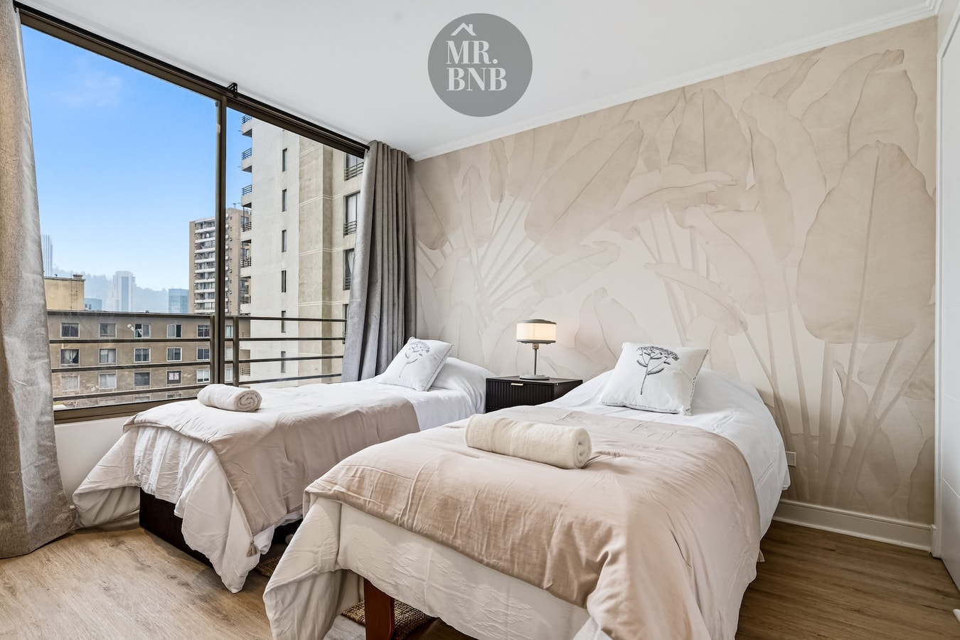 Dormitorio con dos camas individuales y ventanal con vista a edificios