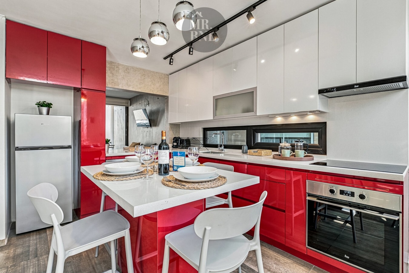 Cocina roja con isla central, mesa puesta y refrigerador