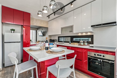 Cocina roja con isla central, mesa puesta y refrigerador