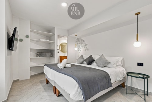 Dormitorio con cama, repisas empotradas y mesa auxiliar junto a la ventana.