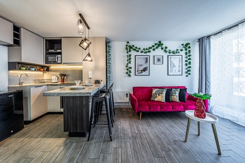Cocina y living integrados desde otro ángulo, mesón central, sofá rojo y ventana con cortina blanca