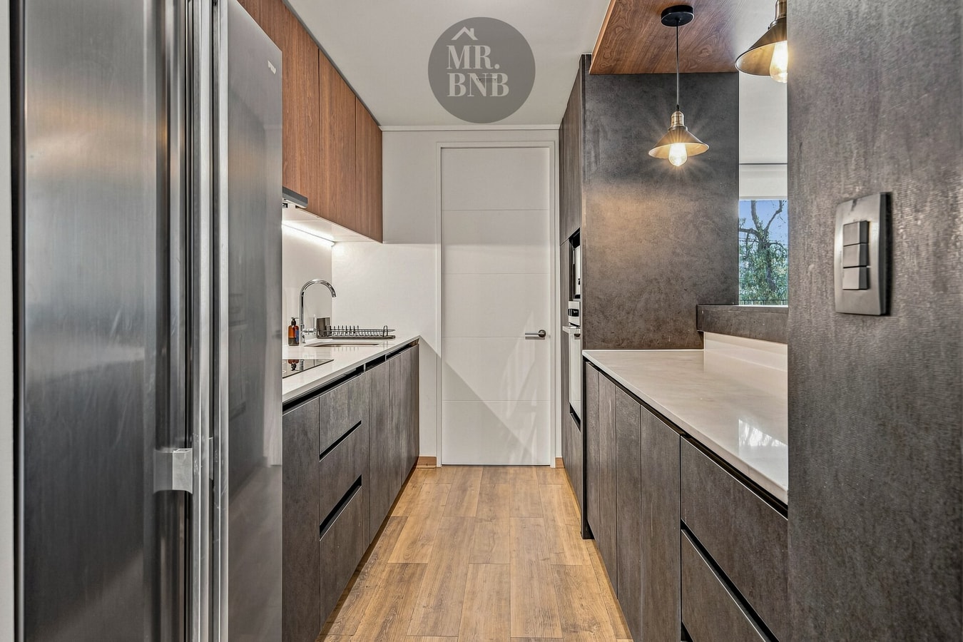 Cocina en línea con muebles oscuros, refrigerador de dos puertas y lavaplatos