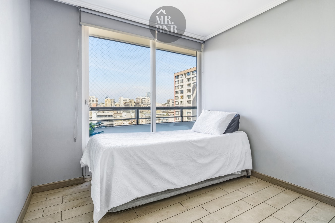 Dormitorio con cama individual y ventanal con vista a edificios