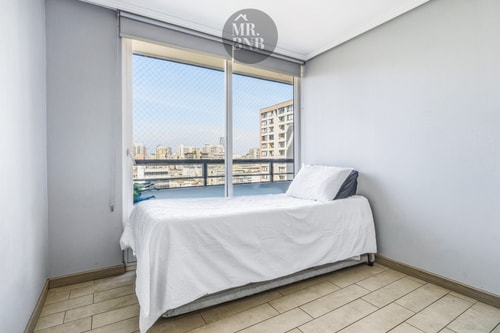 Dormitorio con cama individual y ventanal con vista a edificios