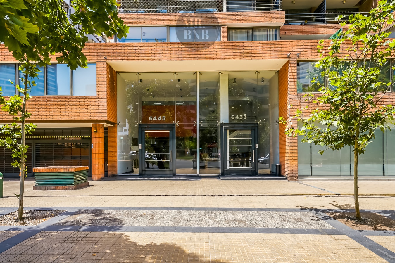 Fachada y acceso del edificio con jardineras y puerta de vidrio.