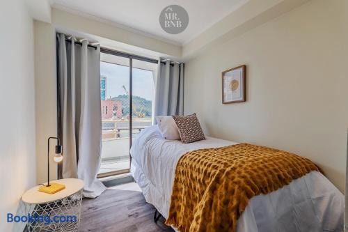 Dormitorio con cama, cubrecama mostaza y ventanal con vista a edificios.