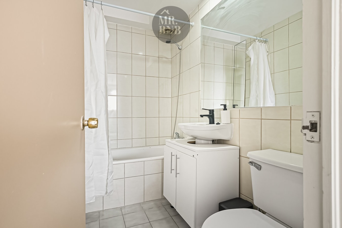 Baño en tonos beige con tina, lavamanos sobre mueble e inodoro