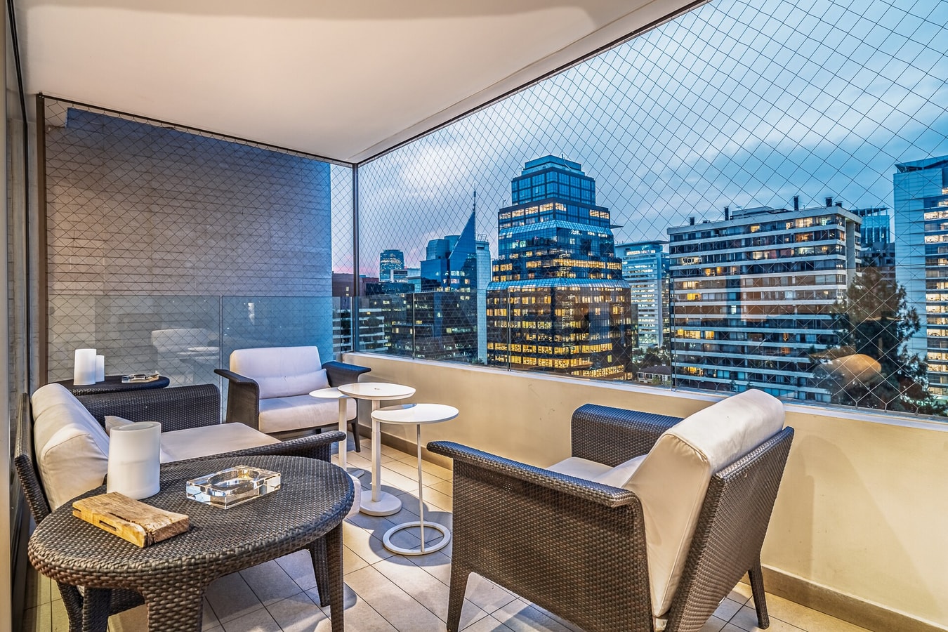 Terraza con mesa y sillones de living, vista nocturna a la ciudad.