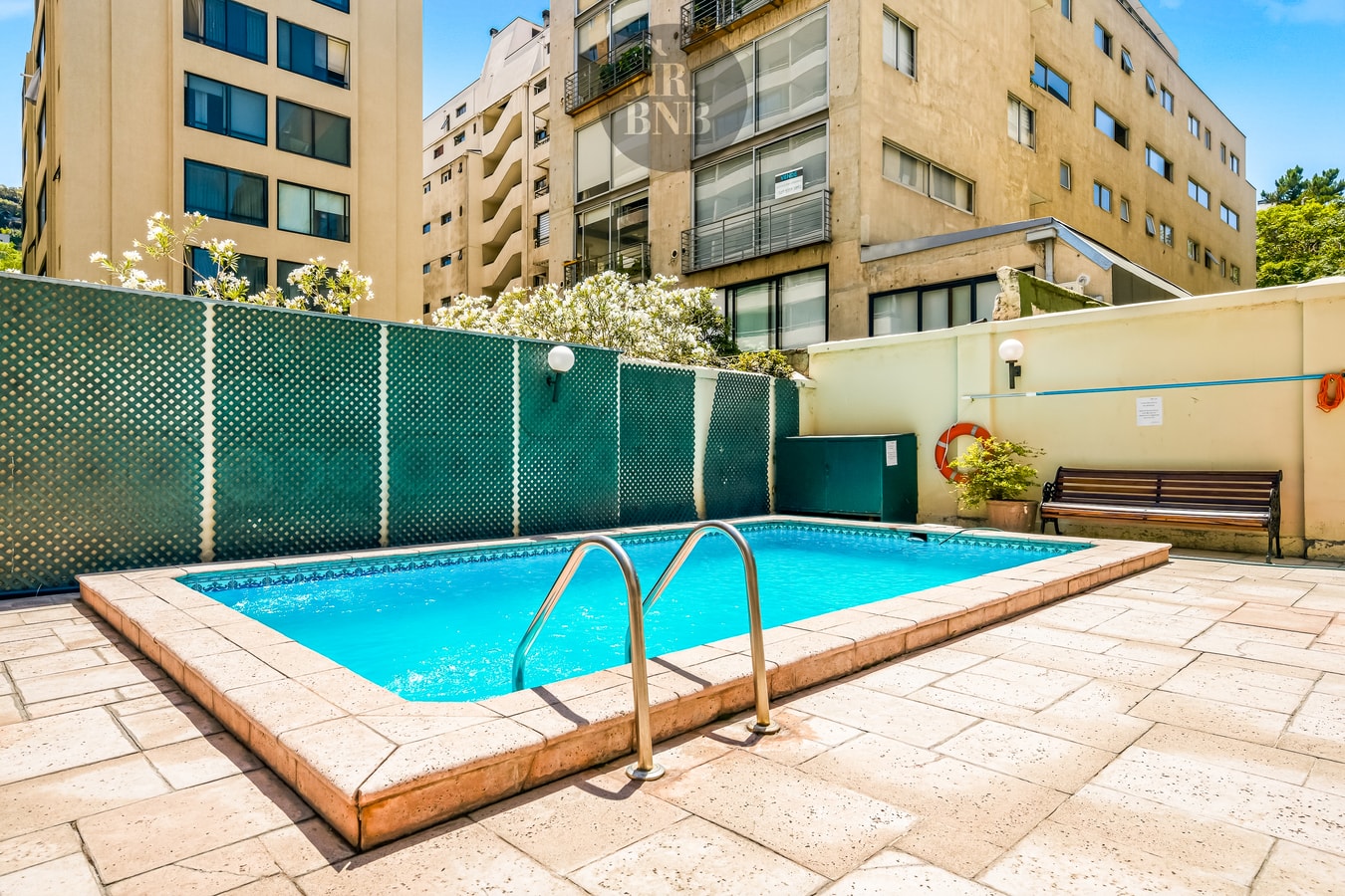 Piscina del edificio en patio exterior, con cerco verde y edificios circundantes de fondo