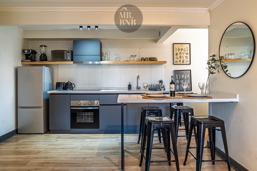 Cocina en ángulo más amplio, con refrigerador, campana y barra con cuatro banquetas altas