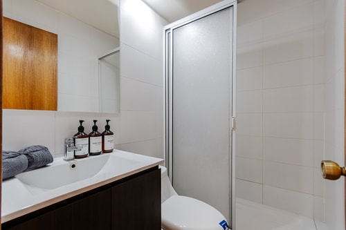Baño con ducha de vidrio, lavamanos y amenities sobre la encimera.
