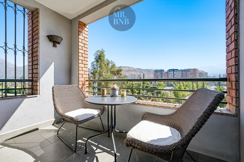 Terraza con mesa redonda y dos sillones, vista panorámica a la cordillera y la ciudad