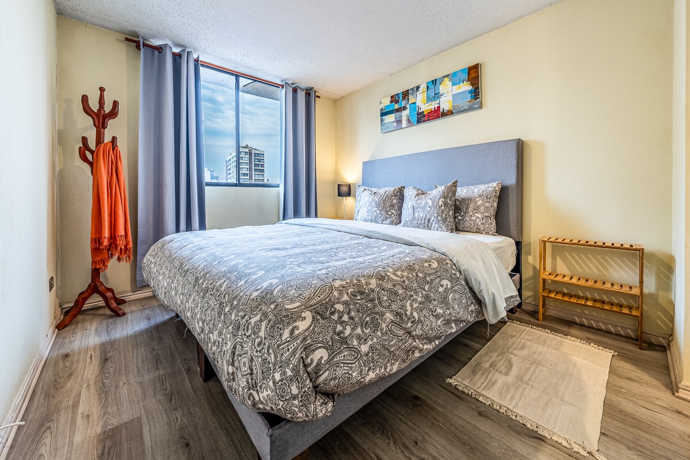 Dormitorio con cama matrimonial, cuadro sobre el respaldo y perchero de pie.