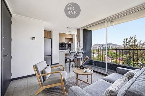 Living con sofá y sillones grises, mesa de centro y ventanal hacia el balcón