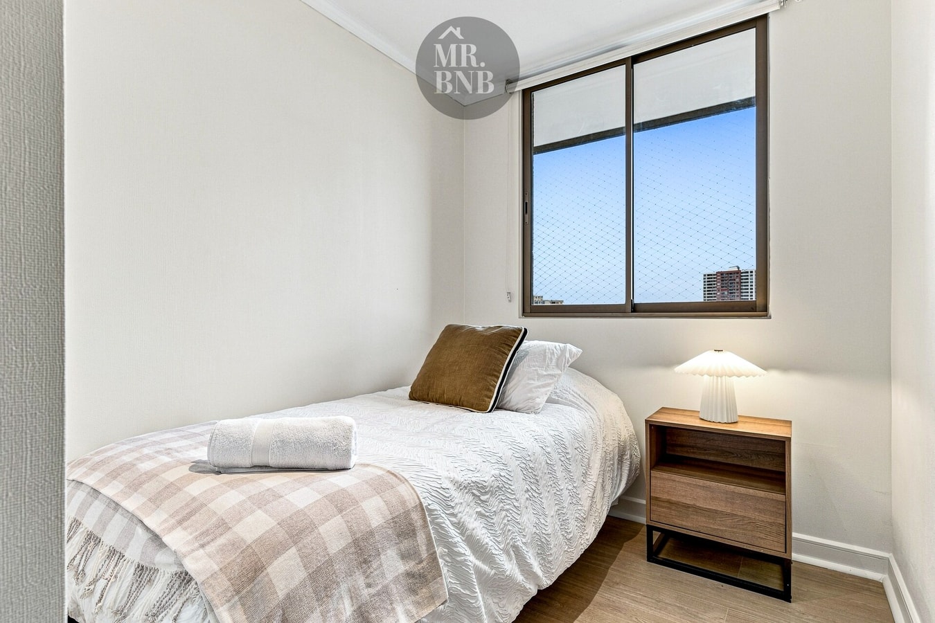 Dormitorio secundario con cama, velador y ventana con vista a edificios