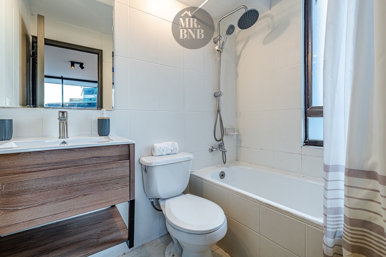 Baño con tina, ducha telefono, lavamanos de madera oscura y espejo